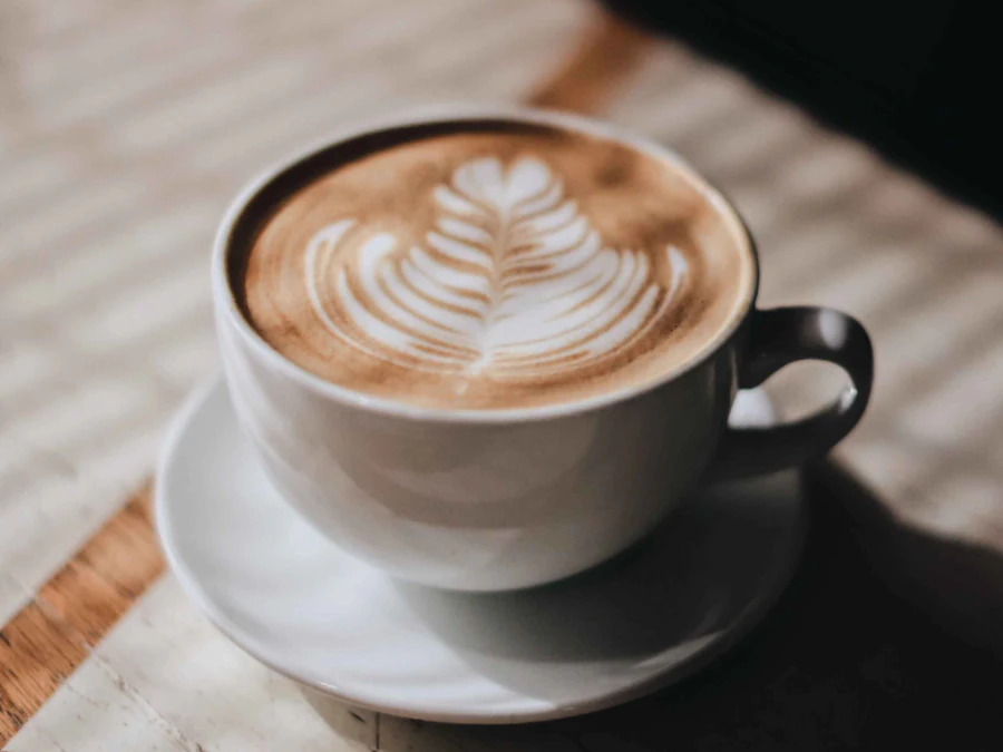 A flat white with latte art in a white cup on a wooden table