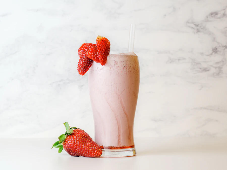 A tall glass of strawberry milk topped with fresh strawberries